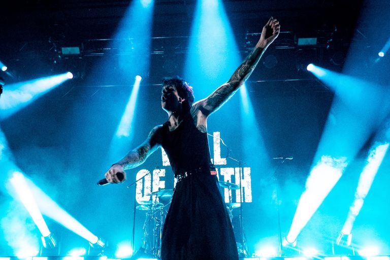 Ocean Sleeper vocalist performing live on stage with arms outstretched under dramatic blue concert lighting and bright stage spotlights.